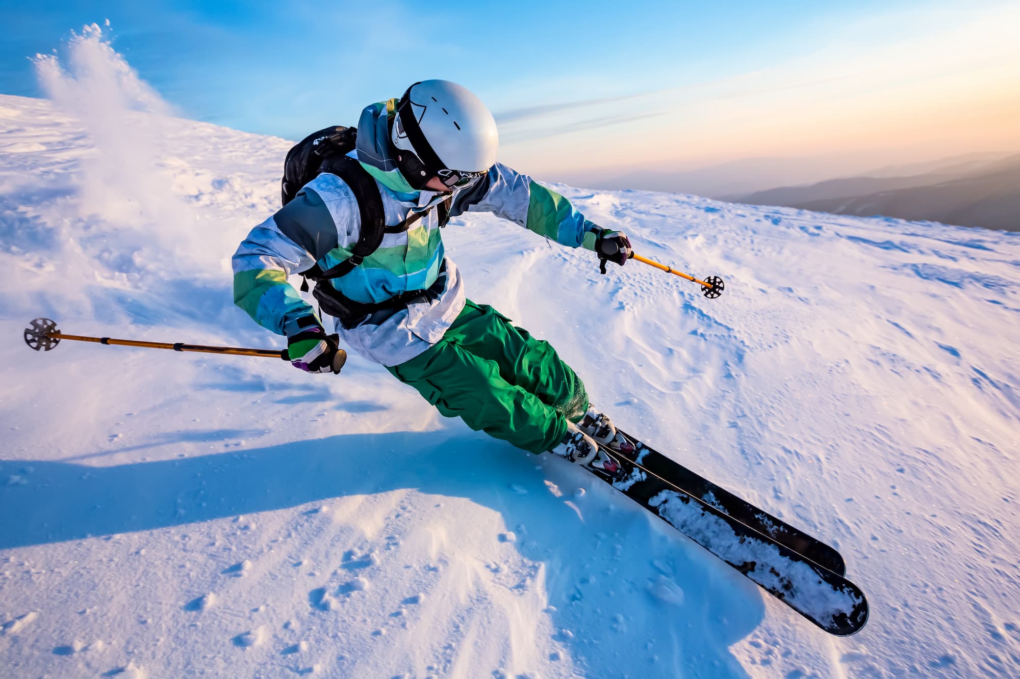 homme en train de faire du ski en montagne avec un équipement complet blanc et vert (casque, ski, bâtons, lunettes, veste, sac à dos, pantalon, bottes, gants)